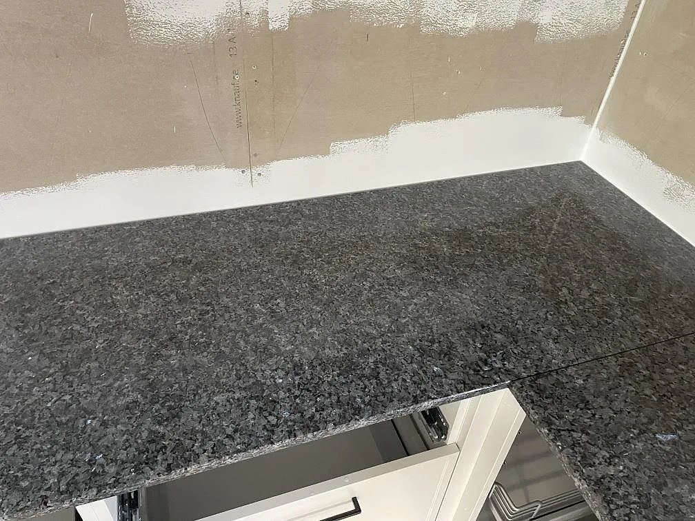 Hörnparti med polerad Blue Pearl granit som köksbänkskiva, monterad mot vägg i ett kök under färdigställande i Sölvesborg.