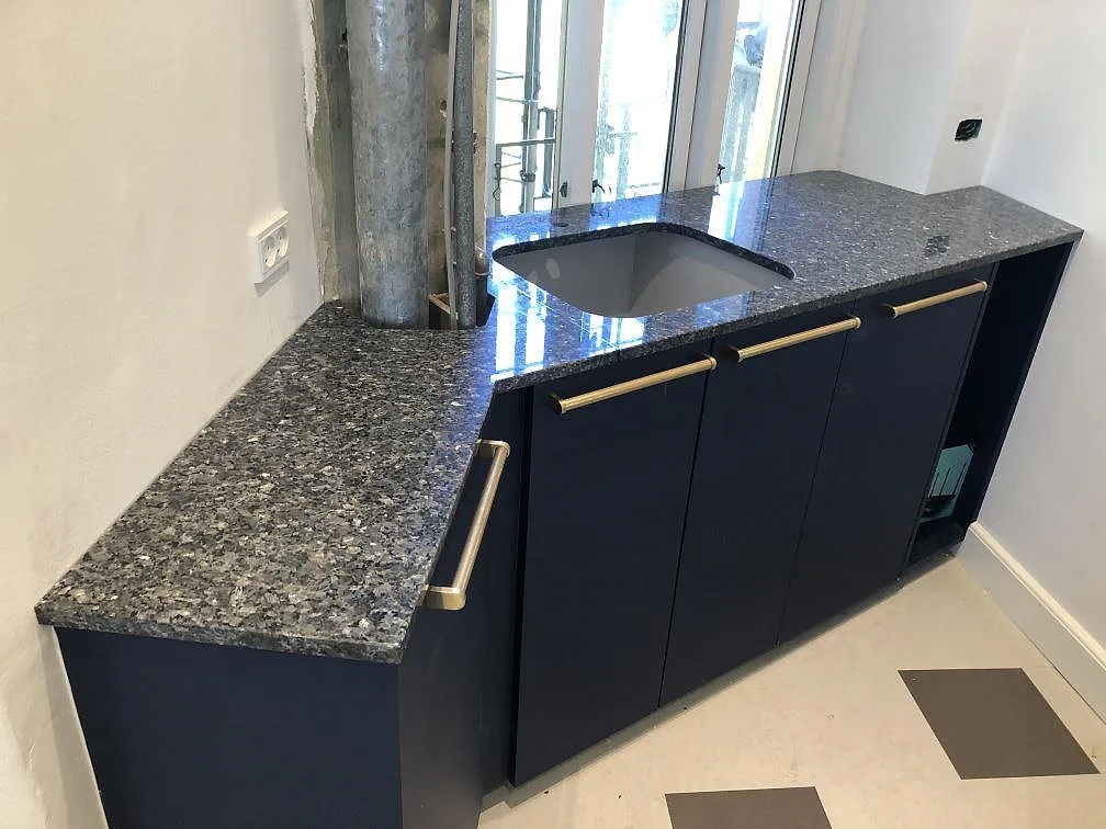 Köksbänkskiva i polerad Blue Pearl granit med underlimmad diskho, mot marinblå köksstommar med mässingshandtag, i ett kök i Valby.