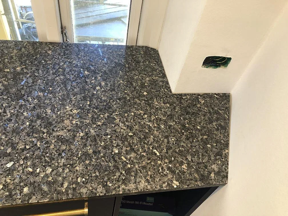 Hörndetalj av polerad Blue Pearl granitbänkskiva med labradoritkristaller mot vit vägg i ett kök i Valby.