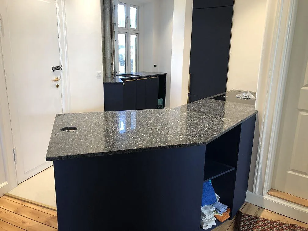 Vinklad köksbänk i polerad Blue Pearl granit med skimrande labradoritkristaller och plats för induktionshäll, under montering i ett kök i Valby.