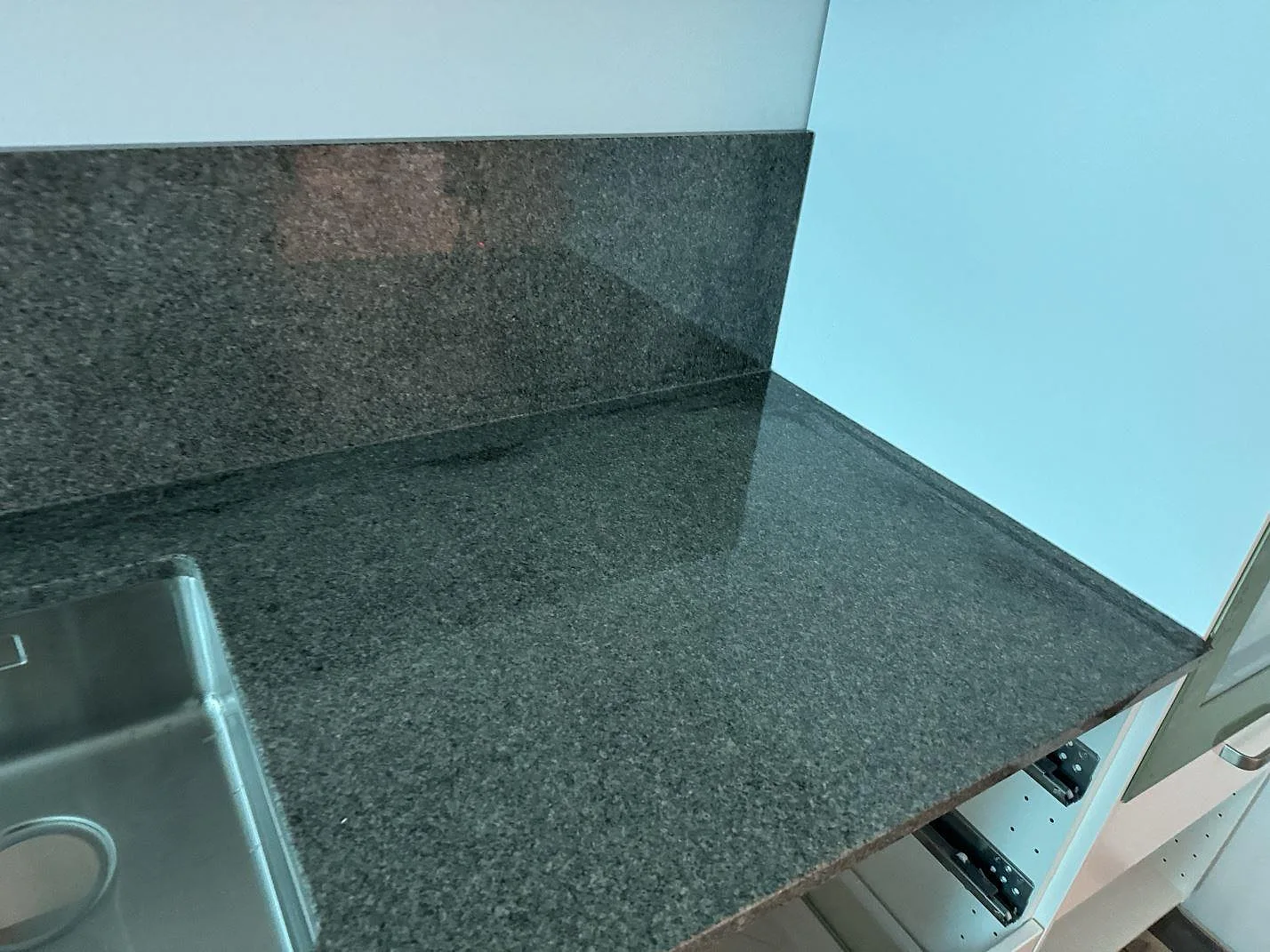 Hörndetalj av polerad Bohus Grå granit med rostfri diskho och uppvikt stänkskydd i Ängelholm.