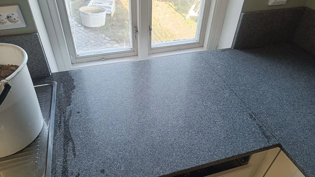 Ytdetalj av 20 mm Bohus Grå granit vid fönsterhörn, med uppvikt stänkkant och blandad finish i Brantevik.