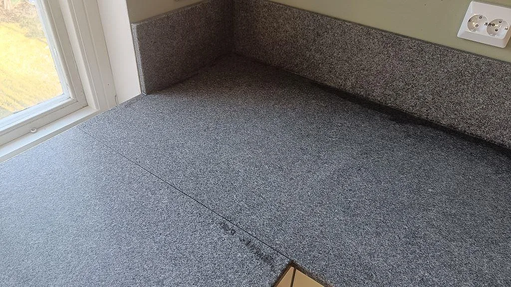 Hörndetalj av köksbänkskiva i Bohus Grå granit med stänkkant och småkornig grå struktur i Brantevik.
