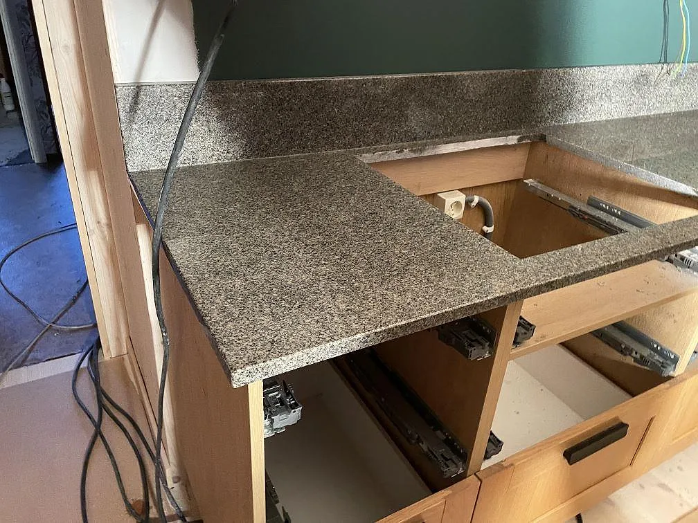 Köksbänkskiva i polerad Bohus Grå granit med diskhåltagning och uppvikt stänkkant mot grön vägg i Dannike.