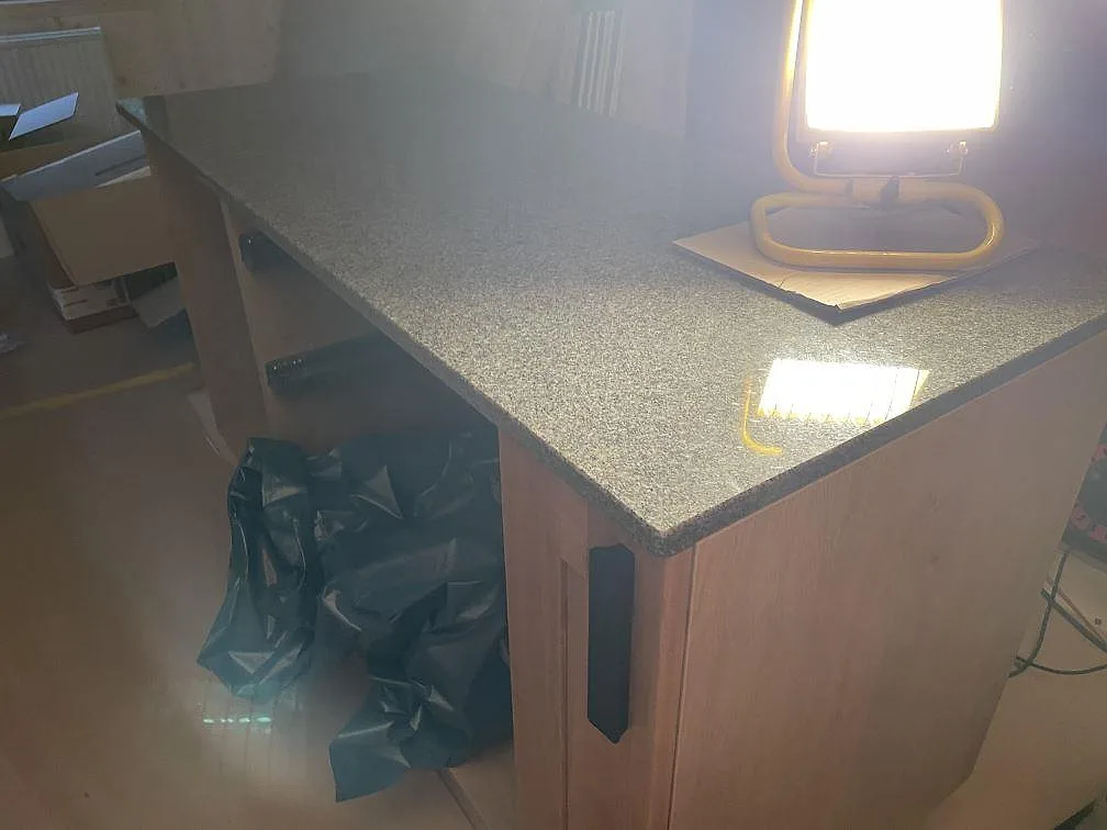 Köksö i polerad Bohus Grå granit med arbetslampa och trästommar under montering i Dannike.