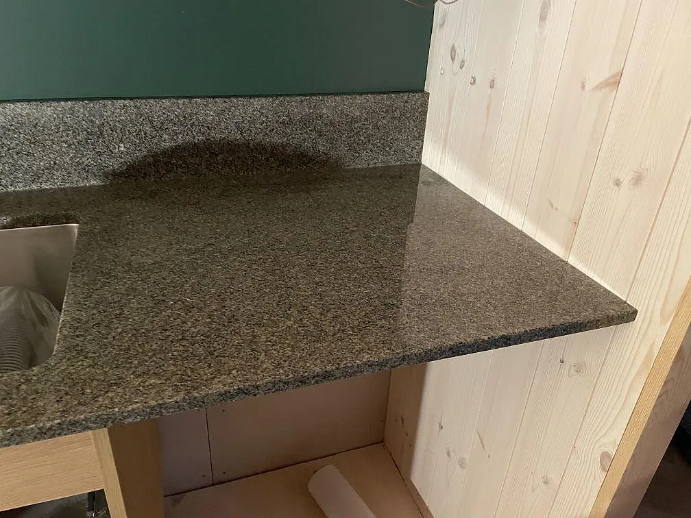 Närbild på polerad Bohus Grå granit vid diskhon, med stänkkant och träpanel i köket i Dannike.
