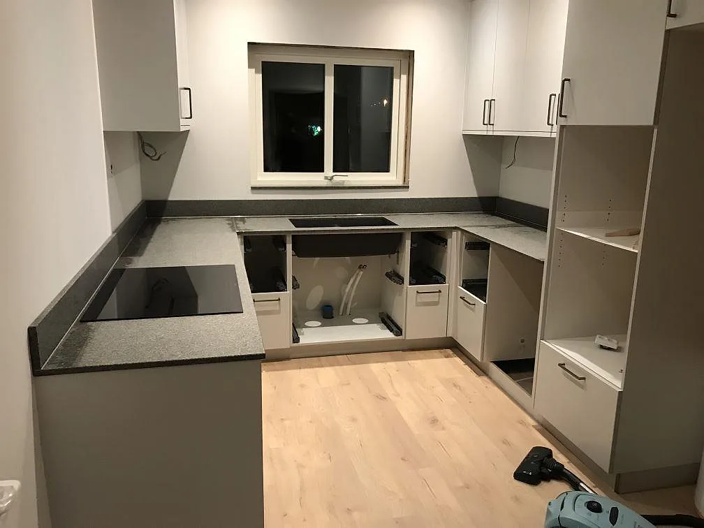 Köksbänkskiva i Bohus Grå granit, matt, i ett U-format kök i Falkenberg med uppvikt stänkkant i samma sten och plats för två induktionshällar.