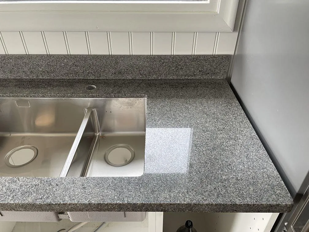 Detalj av polerad Bohus Grå granit runt dubbel rostfri diskho och låg stänkkant i Göteborg.