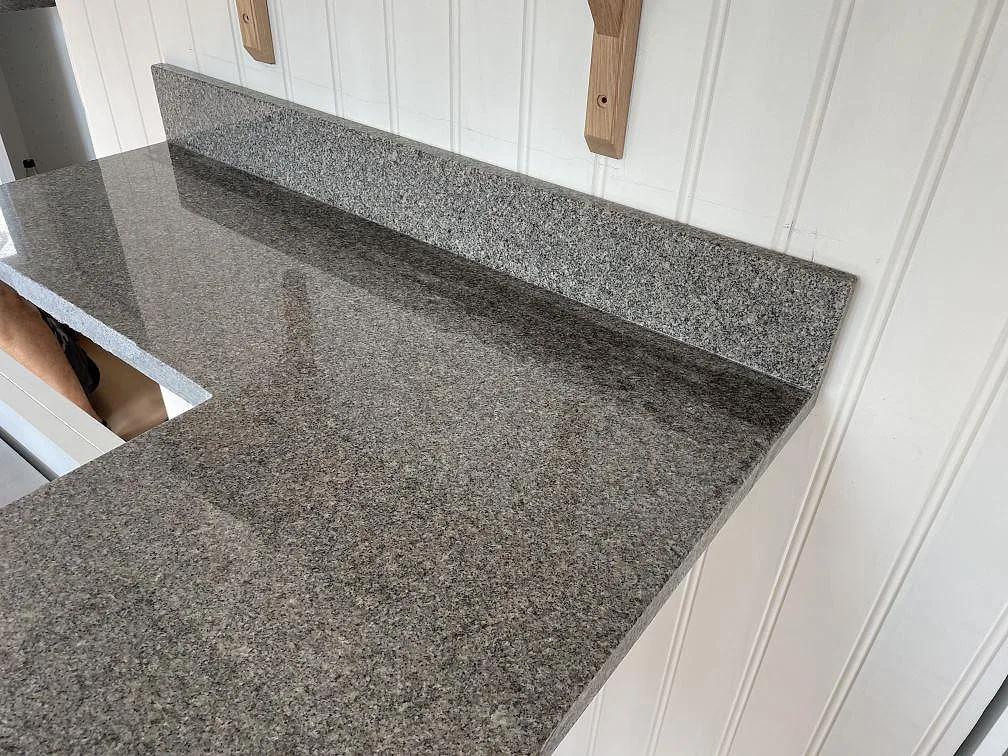 Polerad Bohus Grå granit med uppvikt stänkkant mot vit panel i ett kök i Göteborg.