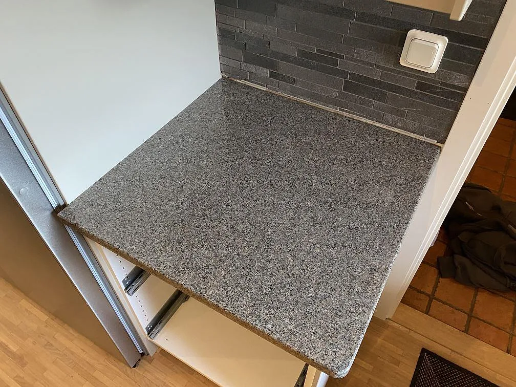Närbild på polerad Bohus Grå granitbänkskiva med rundad kant och mörkt kakel i ett kök i Höör.