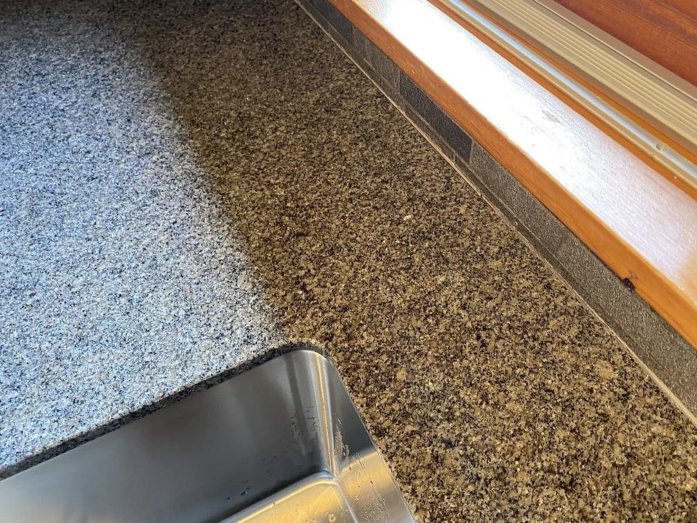 Detaljbild av polerad Bohus Grå granit vid rostfri diskho och fönster i kök i Höör.