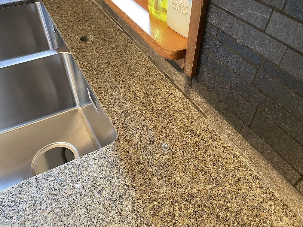 Närbild på polerad Bohus Grå granit runt rostfri diskho, blandarhål och mörkt kakel i Höör.