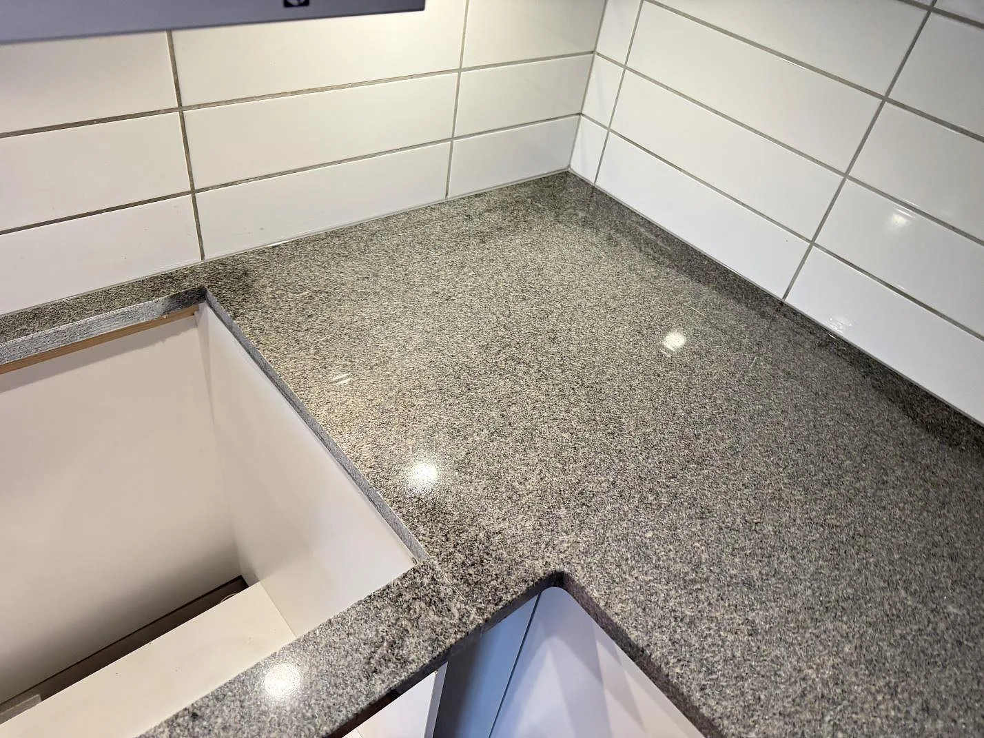 Hörndel av L-formad köksbänkskiva i polerad Bohus Grå granit med vit kakelvägg i Kyrkesund.