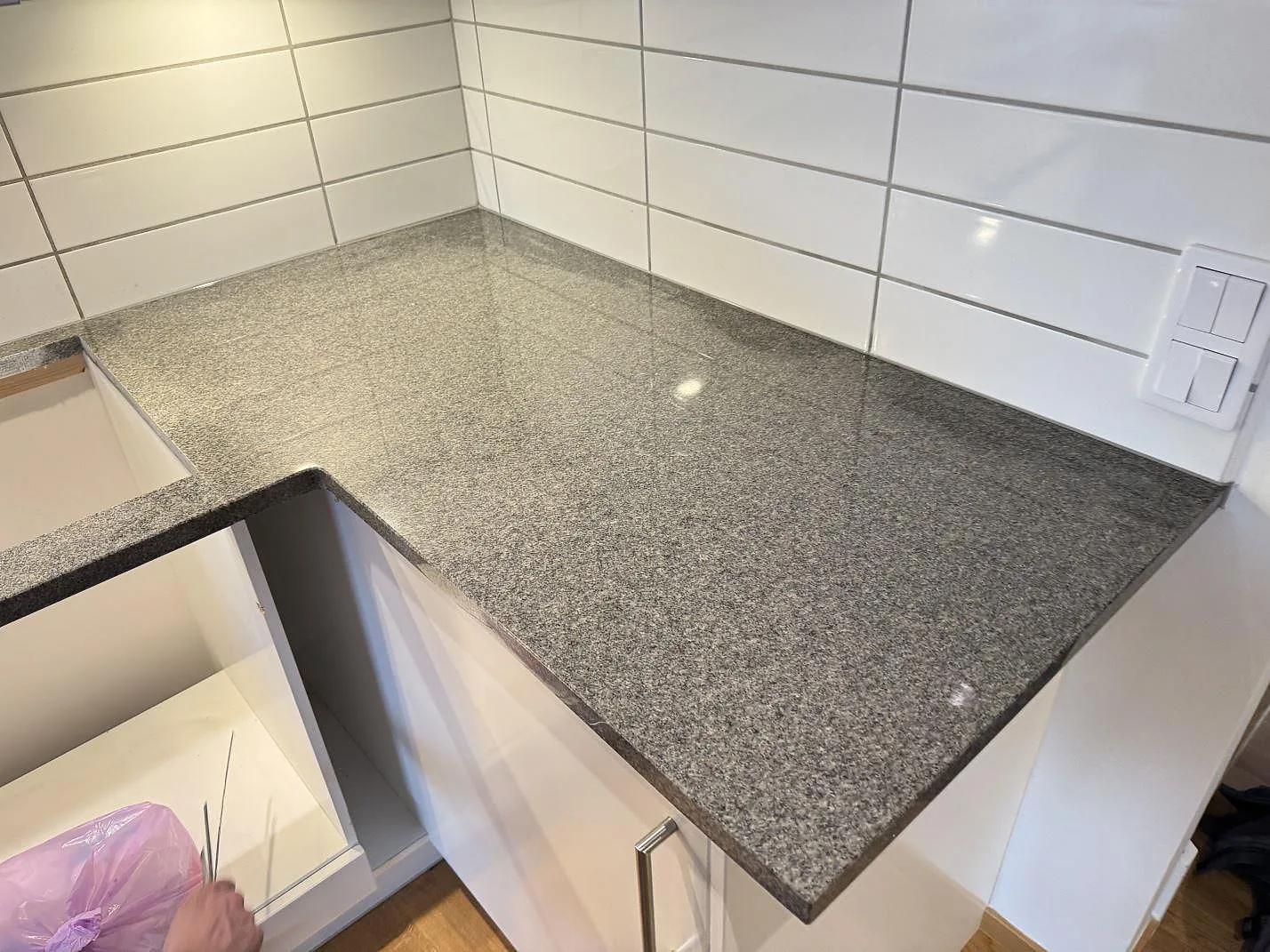 Blank polerad Bohus Grå granit på L-formad köksbänk med ljusa luckor och kakel i Kyrkesund.