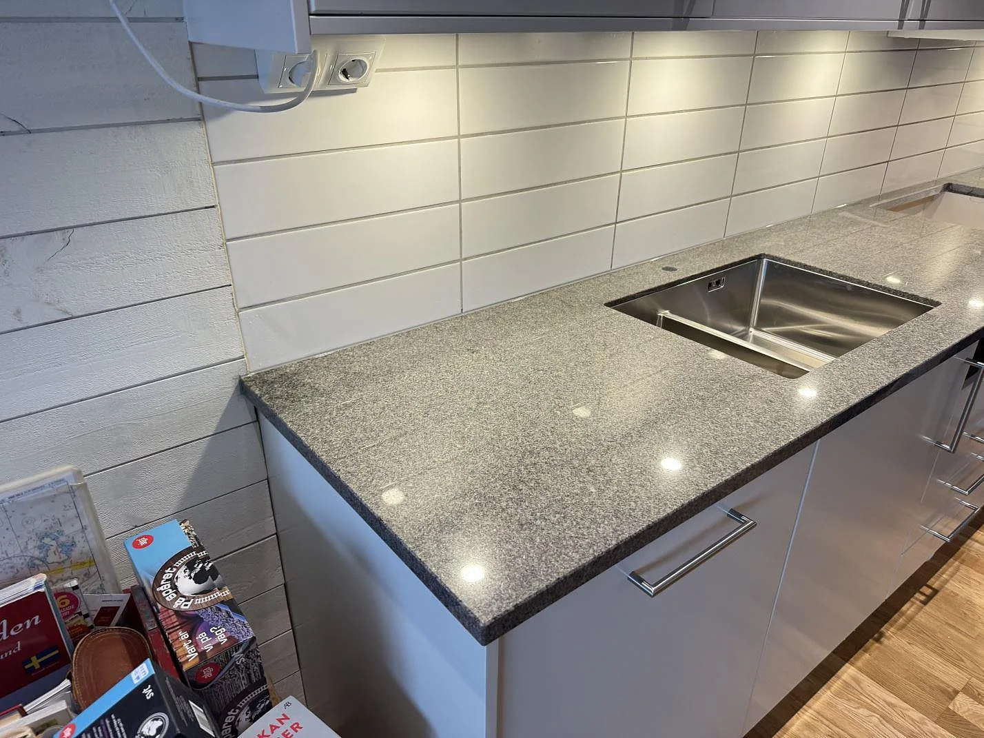 Köksbänkskiva i polerad Bohus Grå granit med rostfri dubbelho och kaklad vägg i ett kök i Kyrkesund.
