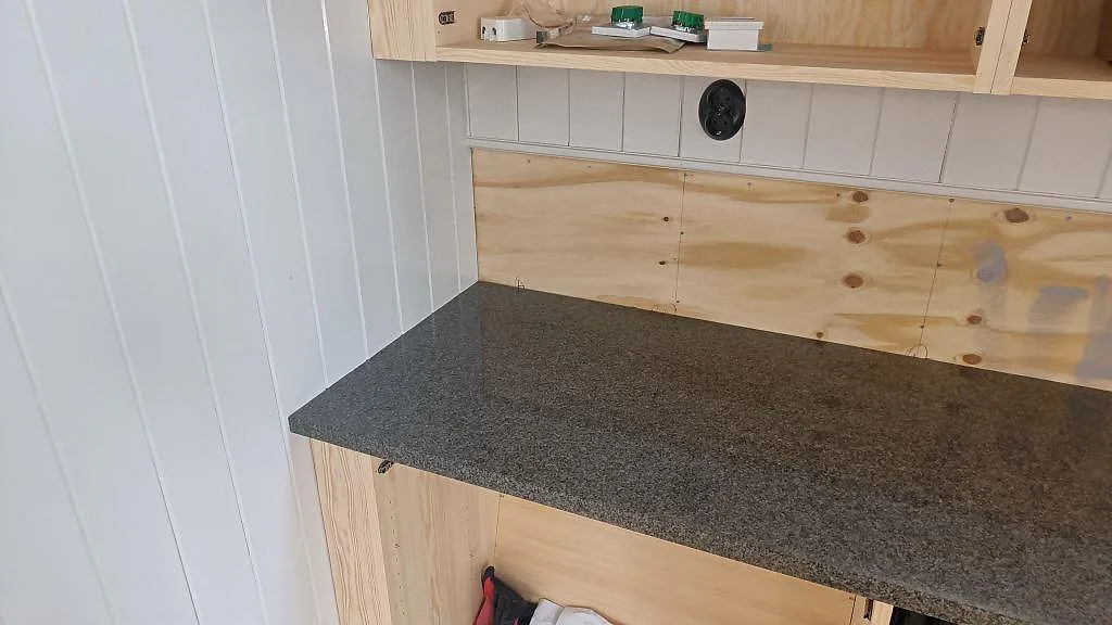 Vänster del av köksbänkskiva i polerad Bohus Grå granit monterad mot vit panelvägg i Landsbro.