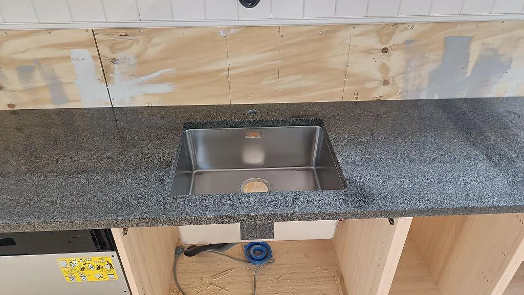 Närbild på rostfri underlimmad diskho i en polerad Bohus Grå granitbänkskiva i Landsbro.