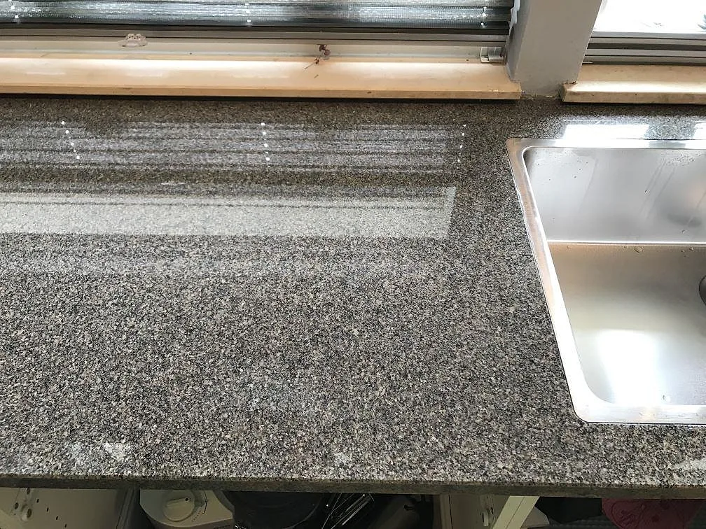 Infälld svart häll i en polerad Bohus Grå granitbänkskiva med vitt kakelstänkskydd i ett kök i Malmö.