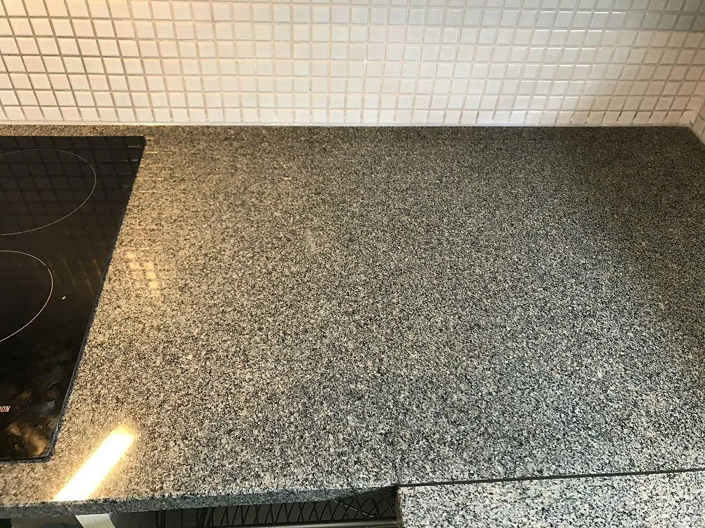 Köksbänkskiva i polerad Bohus Grå granit med stor underlimmad rostfri diskho under fönstret i ett kök i Malmö.