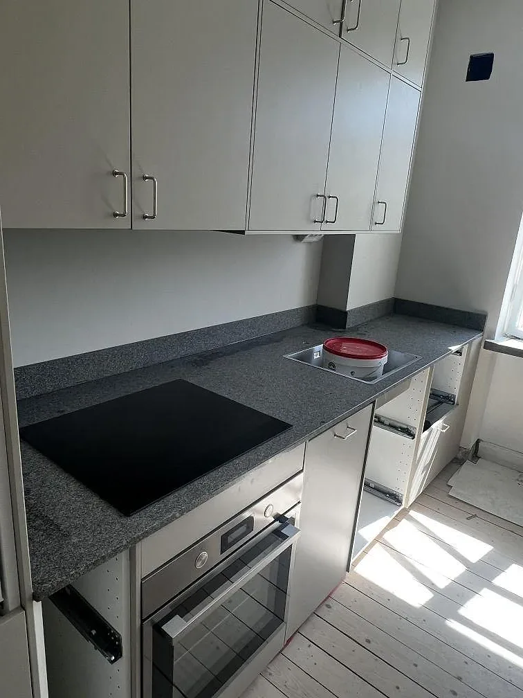 Köksbänkskiva i matt Bohus Grå granit med svart induktionshäll, rostfri diskho och hög stänkvägg i ett kök i Malmö.