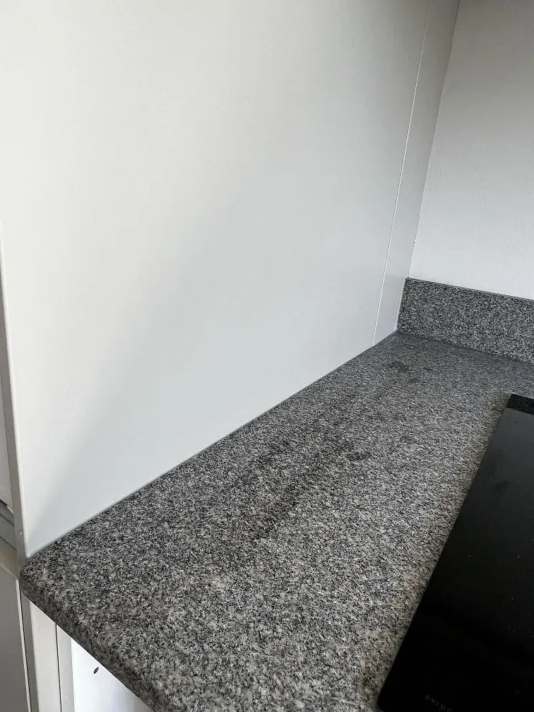 Detalj av matt Bohus Grå granit vid induktionshäll och uppvikt stänkkant i ett vitt kök i Malmö.
