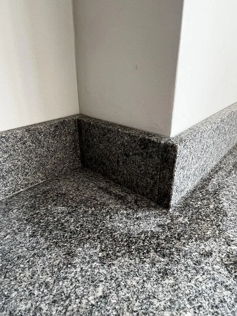 Detalj av väggutsprång och stänkvägg i matt Bohus Grå granit över köksbänken i Malmö.