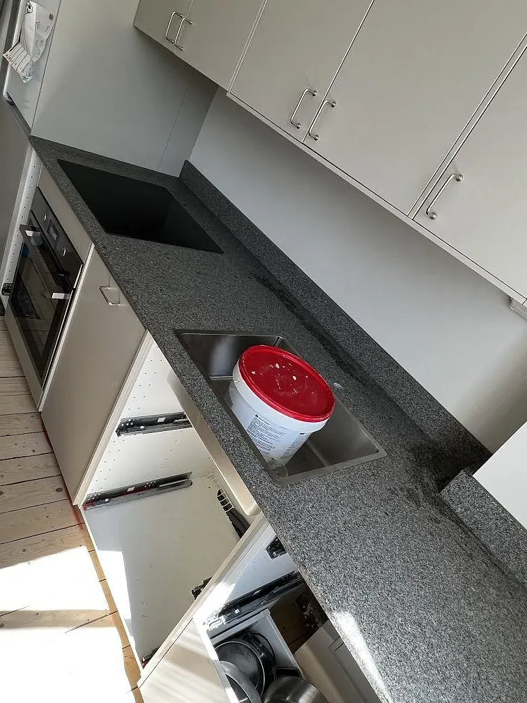 U-format kök i Malmö med matt Bohus Grå granit, vita luckor, svart häll och rostfri diskho under montering.