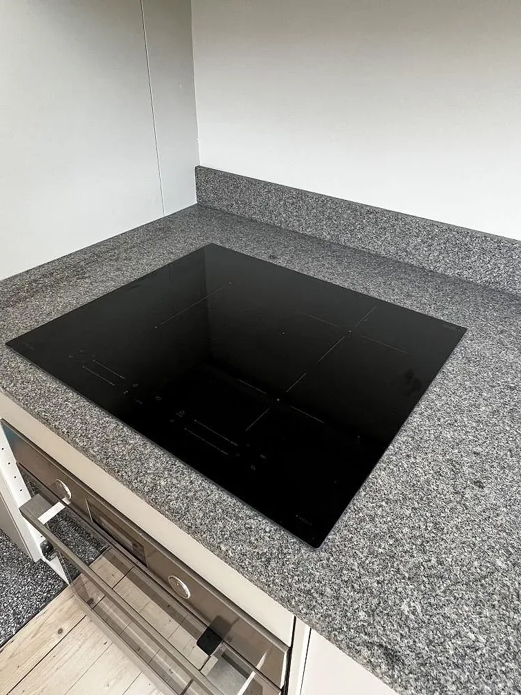 Närbild på svart induktionshäll i en matt köksbänkskiva av Bohus Grå granit med stänkskydd i Malmö.