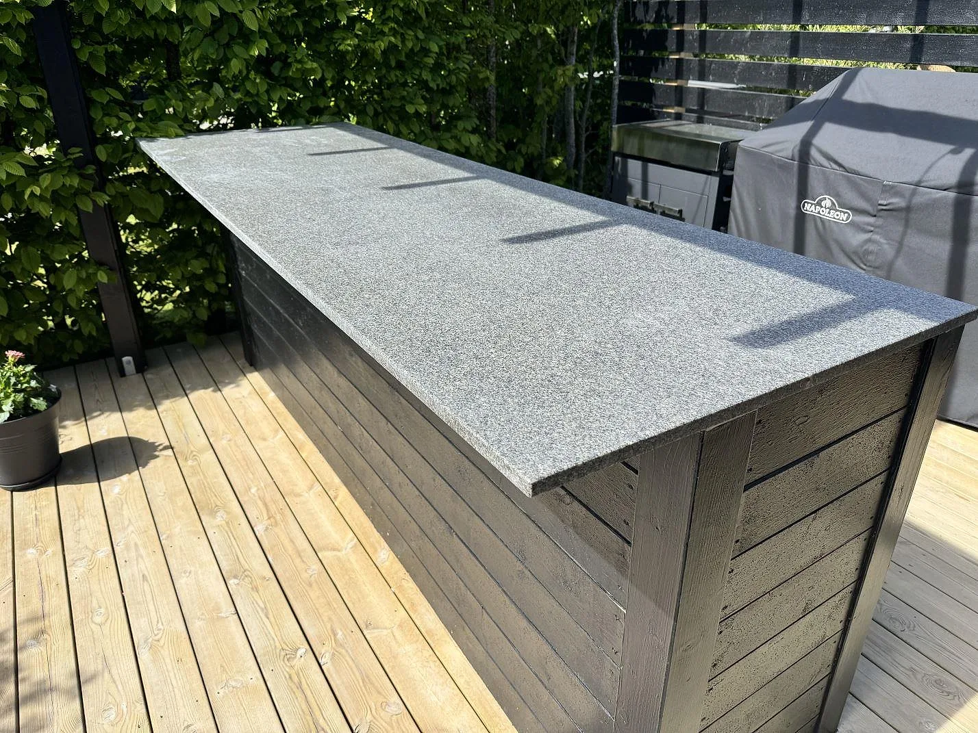 Utekök med lång köksbänkskiva i matt Bohus Grå granit på mörk träinredning och trädäck i Malmö.