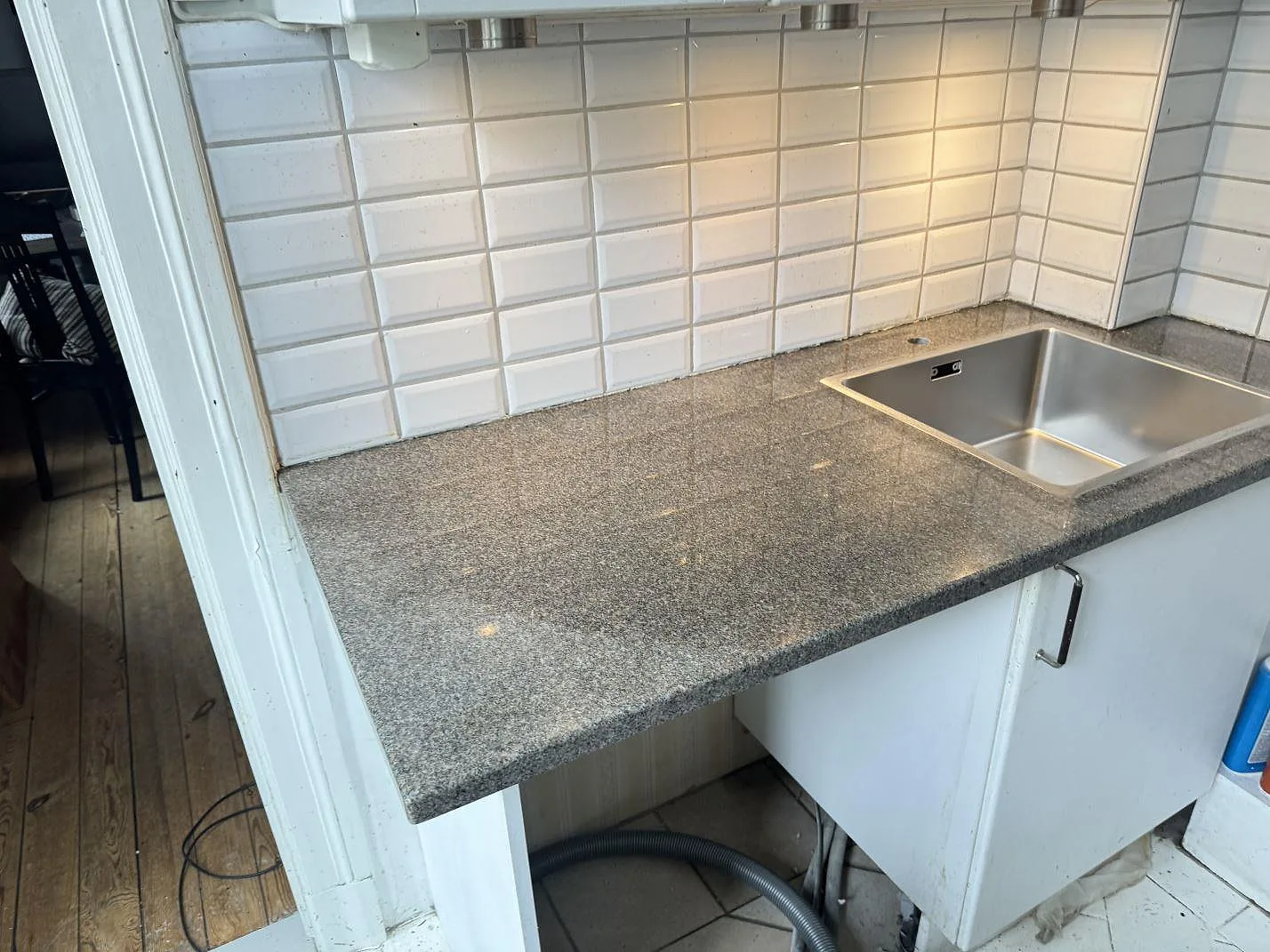 Polerad köksbänkskiva i Bohus Grå granit med rostfri diskho och vit kakelvägg i ett kök i Malmö.
