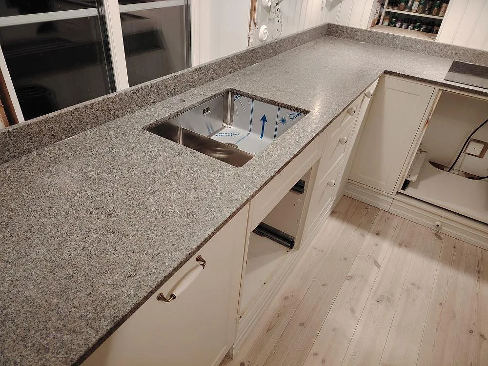 Närbild på matt Bohus Grå granit som köksbänkskiva med stänkkant och synlig diskho i ett kök i Mockfjärd.
