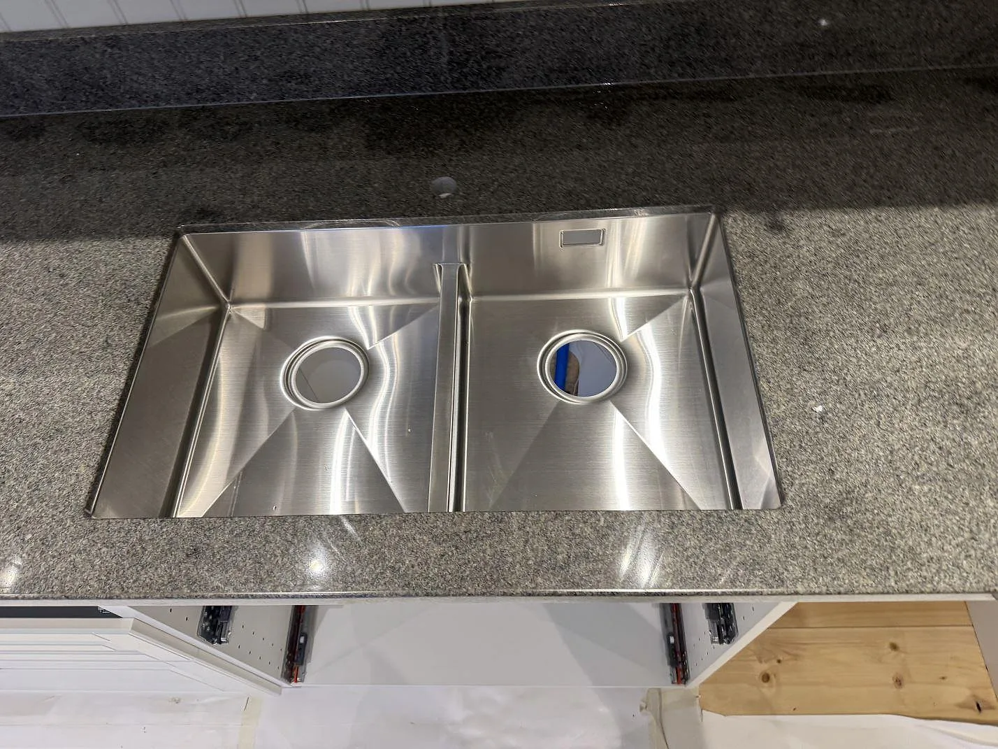 Detalj av polerad Bohus Grå granit runt en rostfri dubbelho i ett kök under montering i Säffle.