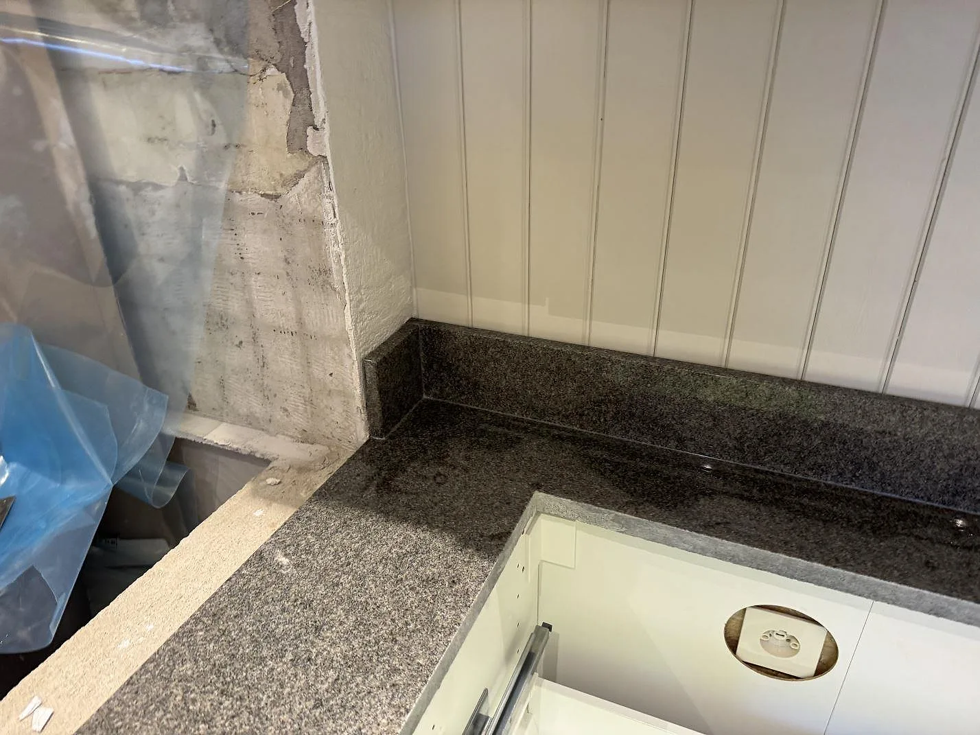 Polerad Bohus Grå granit med låg stänkkant vid väggpanel och öppna stommar i ett kök under montering i Säffle.