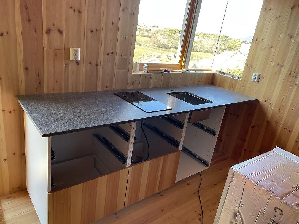 Köksbänkskiva i grå Bohus Grå-granit, matt yta, monterad som vinklad köksbänk med induktionshäll och underlimmad diskho i ett träklätt kök i Skärhamn.