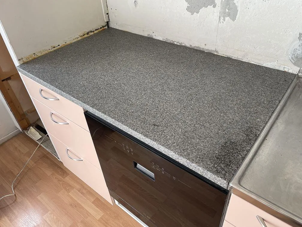 Matt köksbänkskiva i Bohus Grå granit, 30 mm, monterad över ljusa lådor i ett kök i Solna under montering.