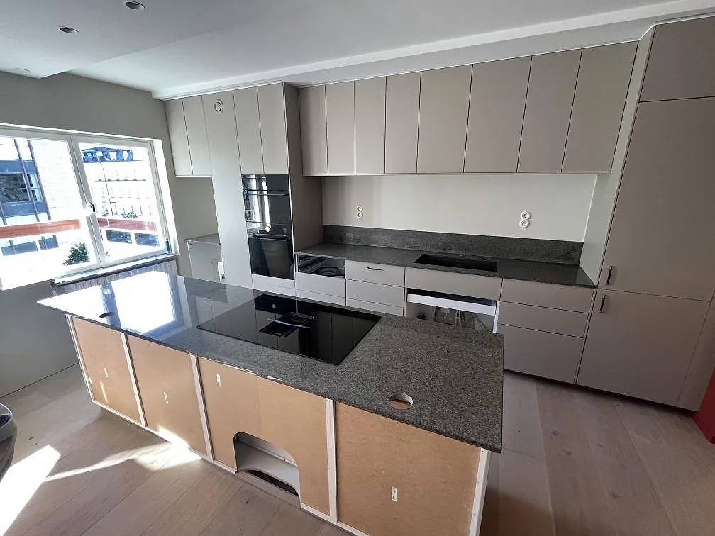 Köksbänkskiva och stor köksö i polerad Bohus Grå granit med svart induktionshäll i ett kök i Stockholm.