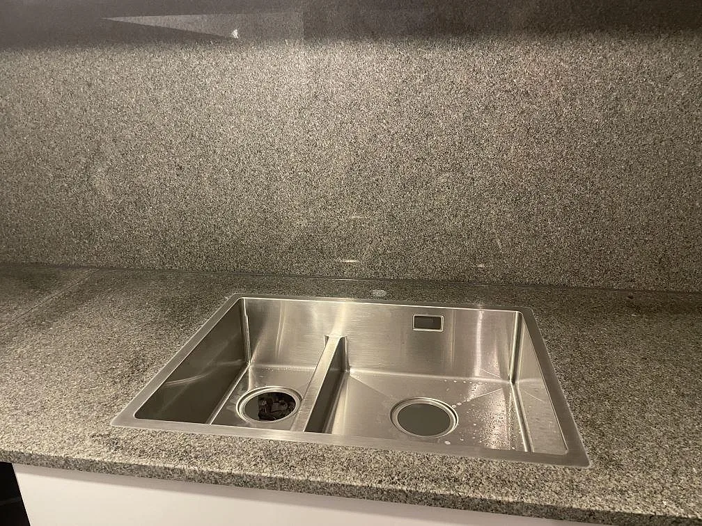 Underlimmad rostfri dubbeldiskho i en polerad köksbänkskiva av Bohus Grå granit i ett kök i Stockholm.