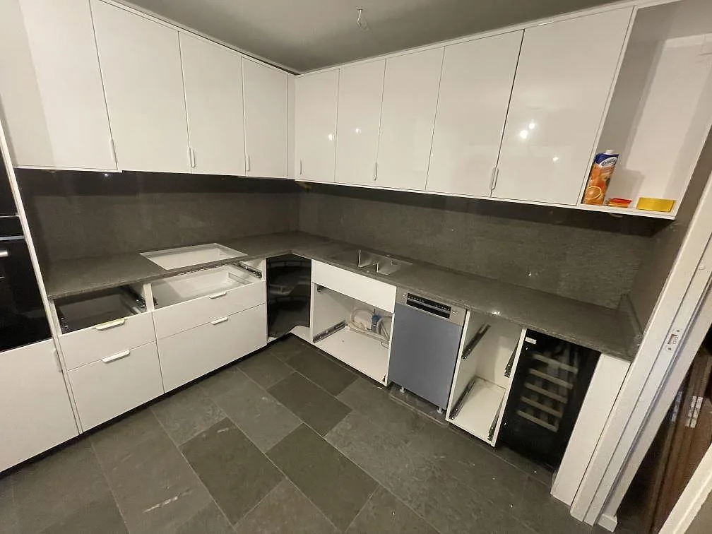 Polerad köksbänkskiva och uppvikt stänkkant i Bohus Grå granit i ett vitt högblankt kök i Stockholm, fotograferat under montering.