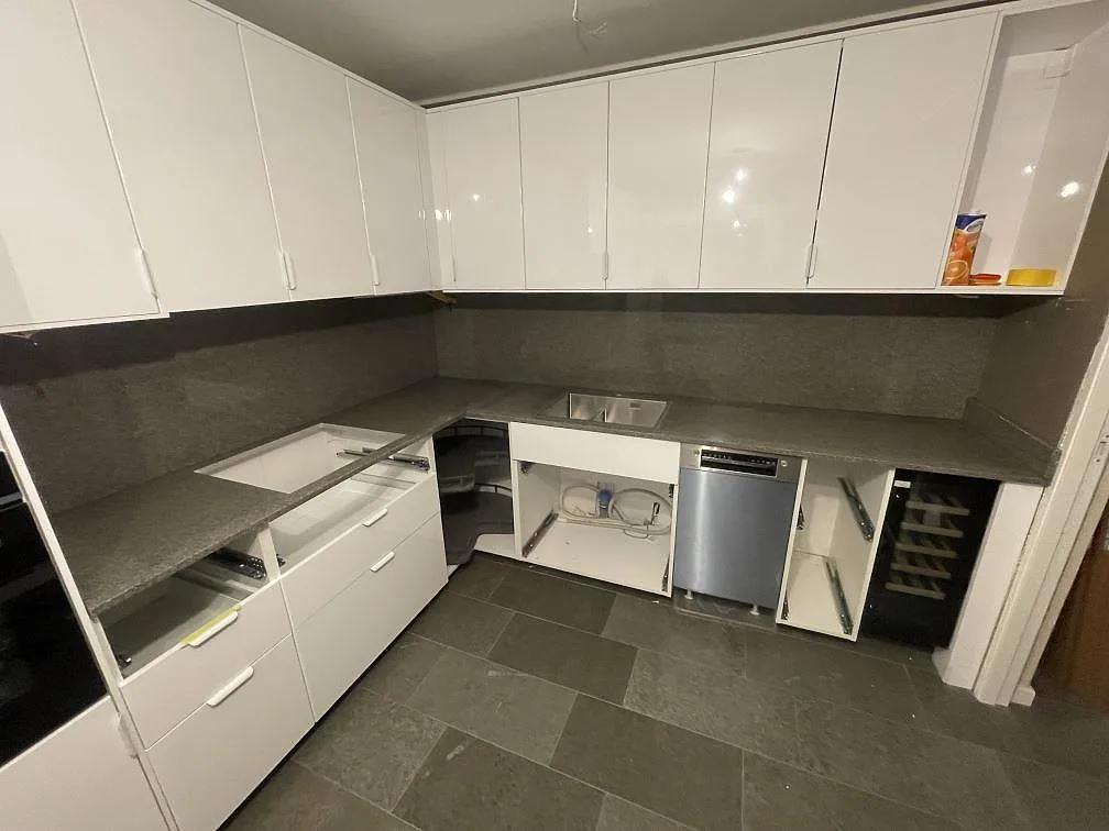 Köksbänkskiva i Bohus Grå granit med underlimmad rostfri diskho i ett vitt kök i Stockholm, med öppna stommar under pågående montering.