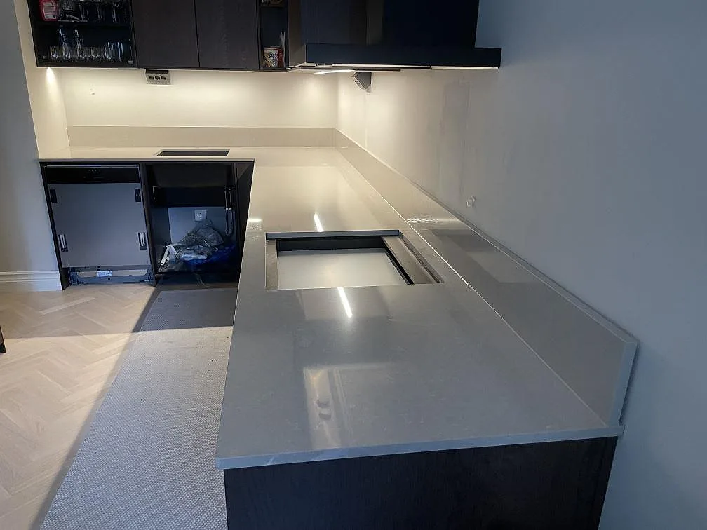 Köksbänkskiva i Bohus Grå granit, polerad 20 mm, längs en vinklad köksuppställning med urtagning för häll i ett kök i Stockholm under montering.