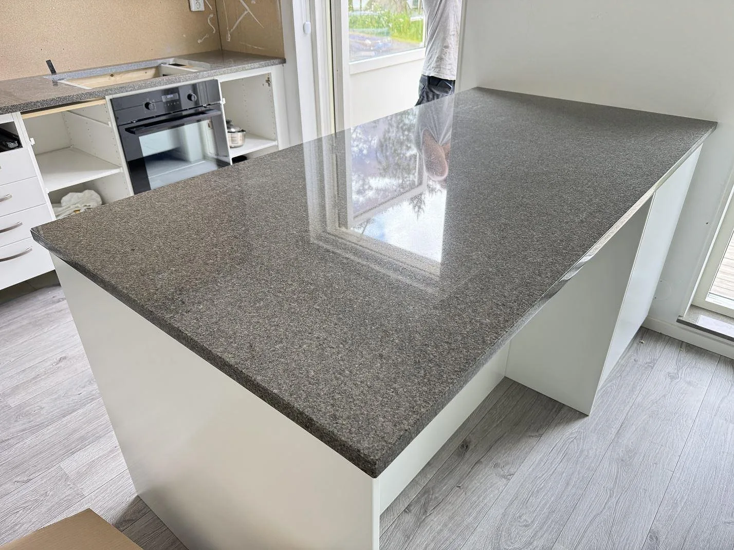 Köksö i polerad Bohus Grå granit, 30 mm, monterad i ett kök i Tenhult med vit köksinredning.