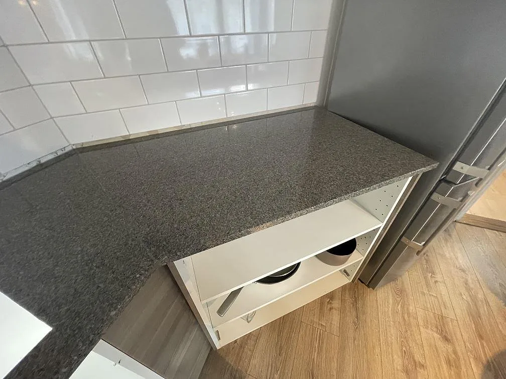 Köksbänk i polerad Bohus Grå granit vid högskåp och kaklad vägg, fotograferad under montering i Upplands Väsby.