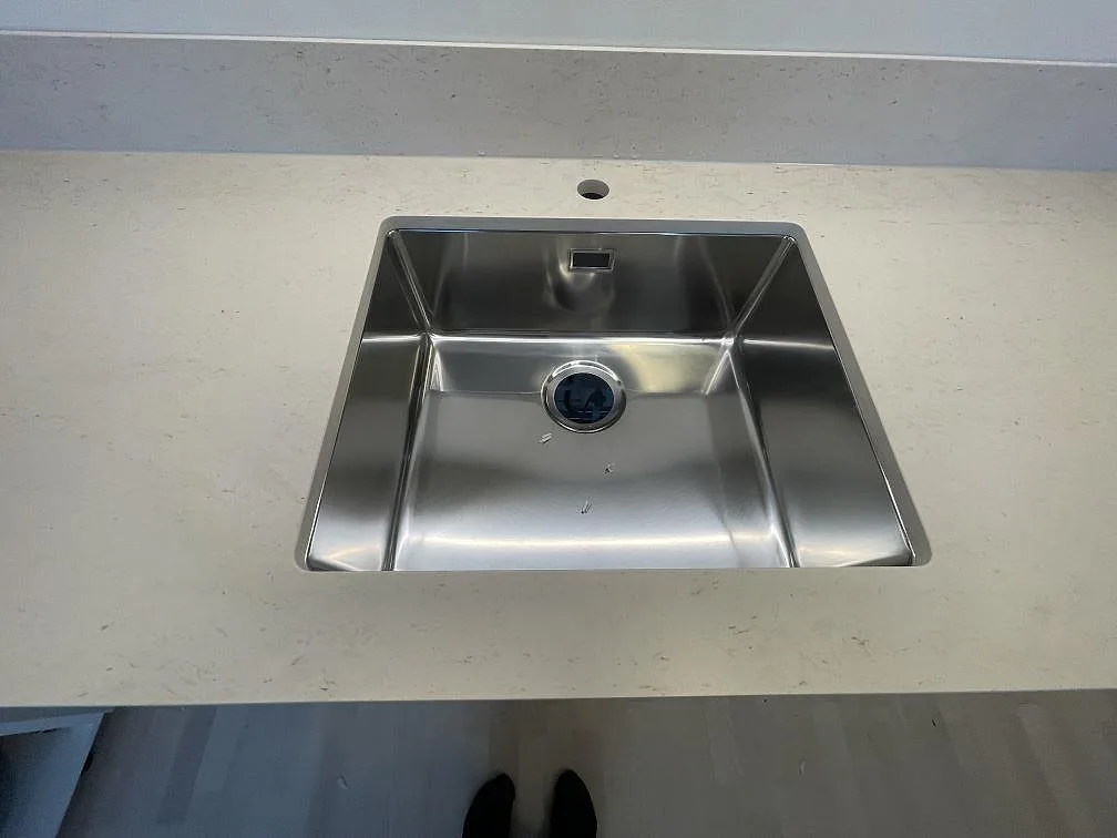 Närbild på polerad Bohus Grå granit med monterad rostfri diskho och låg stänkkant i ett kök i Upplands Väsby.