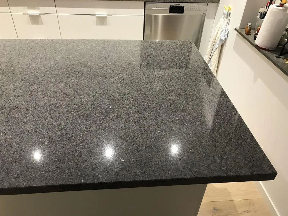 Köksbänkskiva och köksö i grå Bohus Grå-granit, polerad, i ett kök i Växjö med vita stommar och infällda spotlights.