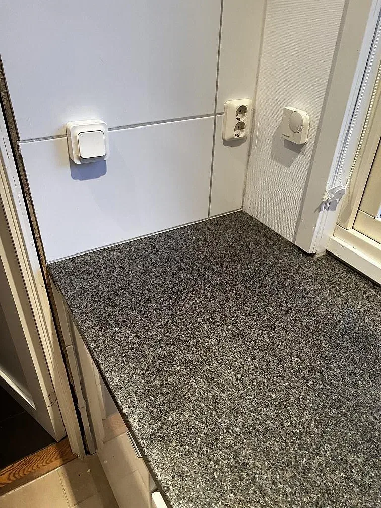 Hörndel av köksbänkskiva i polerad Bohus Grå granit mot vita skåp och fönster i Växjö.