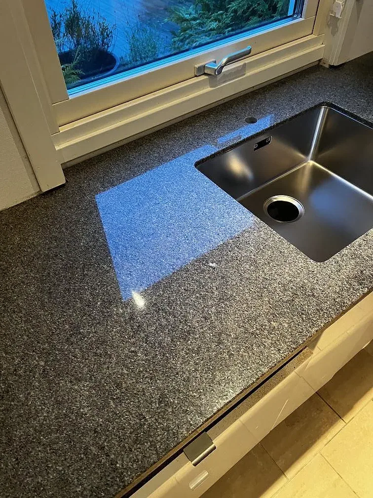 Köksbänkskiva i Bohus Grå granit, polerad, med rostfri diskho vid fönster i ett kök i Växjö.