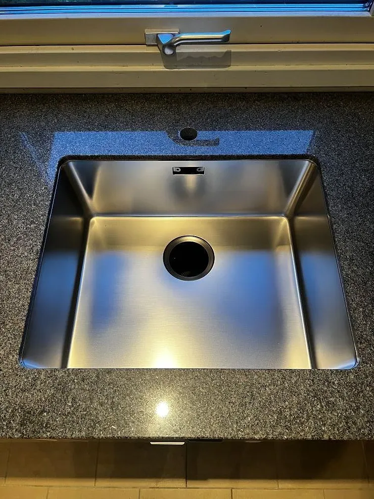 Närbild på rostfri diskho ovanpå en polerad köksbänkskiva i Bohus Grå granit i Växjö.