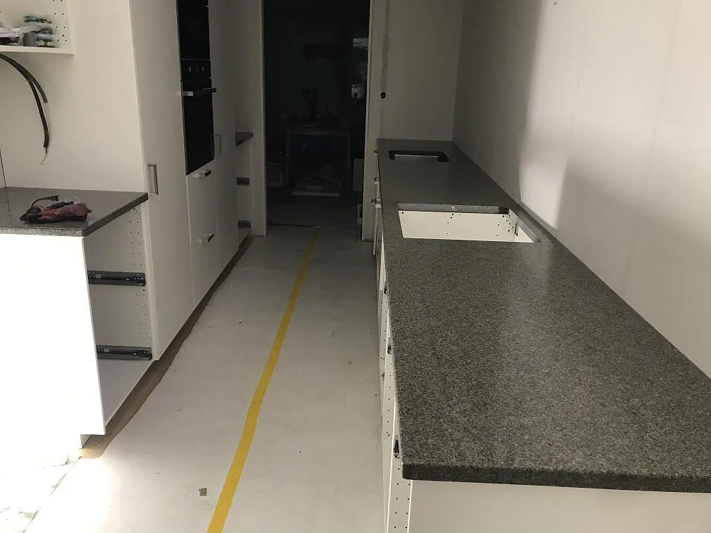 Lång köksbänkskiva i grå Bohus granit, polerad, längs ett kök under montering i Varberg med urtag för diskho och häll.