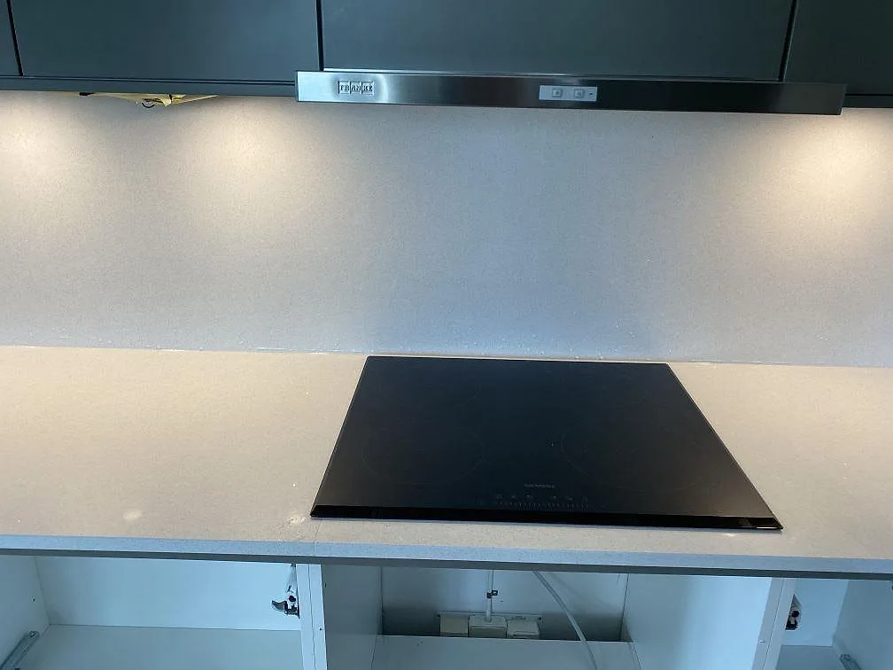 Polerad vit Brilliant White köksbänkskiva med infälld svart induktionshäll och dova grå överskåp i ett kök i Malmö.