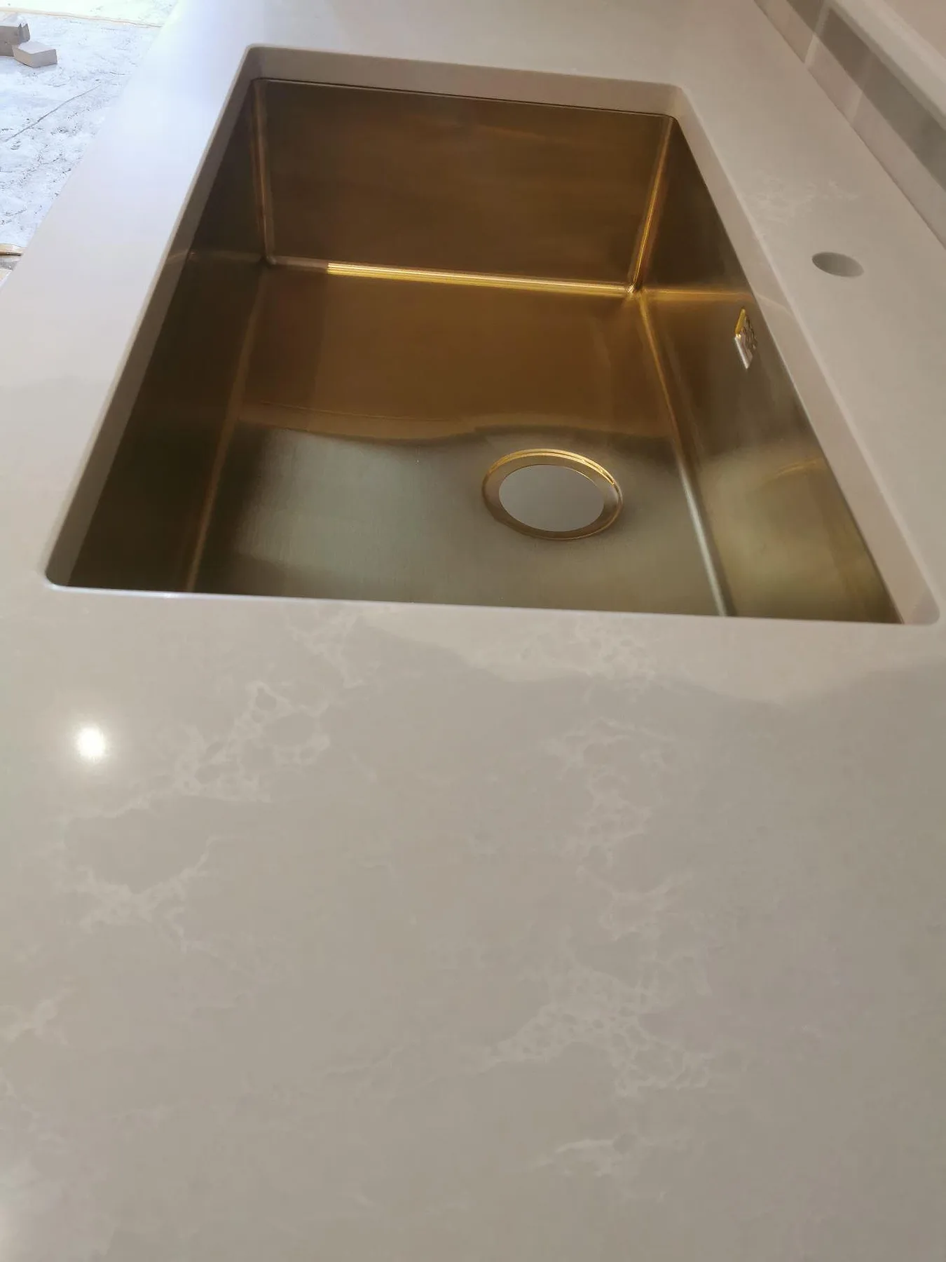 Köksbänkskiva i vit Caesarstone Alpine Mist, polerad kvartskomposit med mjuk grå ådring, med underlimmad diskho i mässingston och borrat blandarhål i ett kök i Ekerö.
